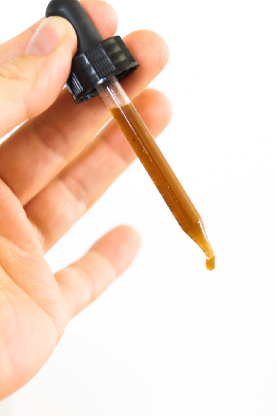 Hand holding McPhees Bees propolis tincture full dropper with drip. 
